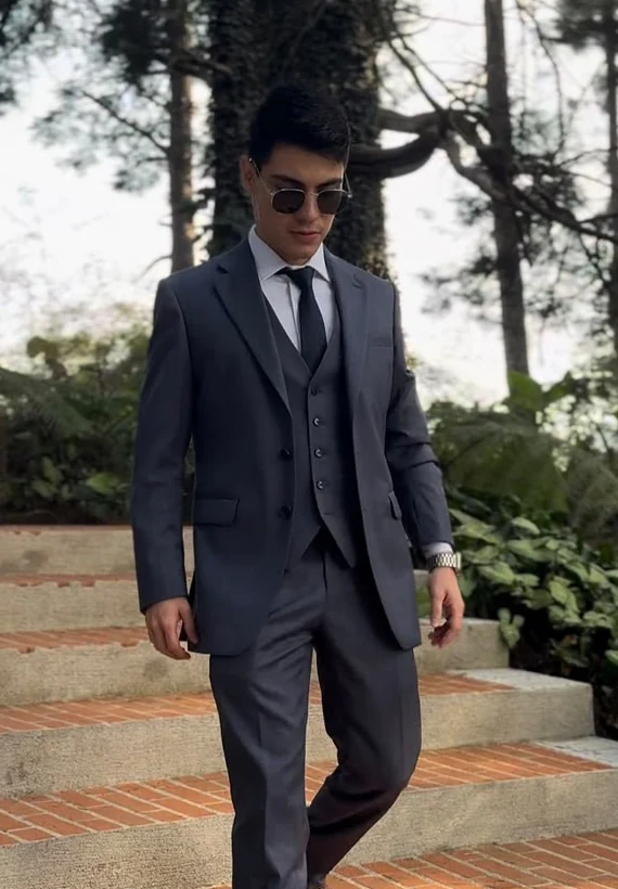 Diego Velásquez, con traje oscuro y gafas, en un entorno natural con árboles y escalinatas.
